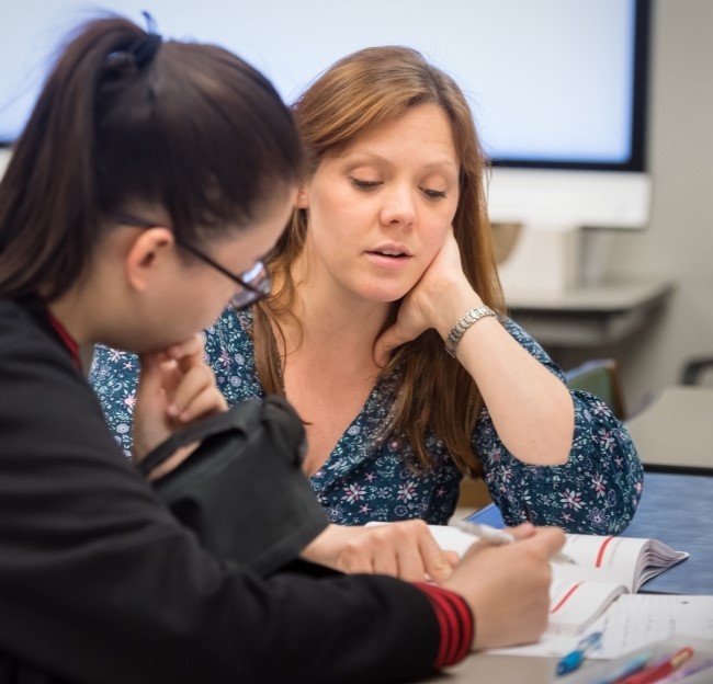 image of teacher and a student seated together and working with a book on a table in front of them