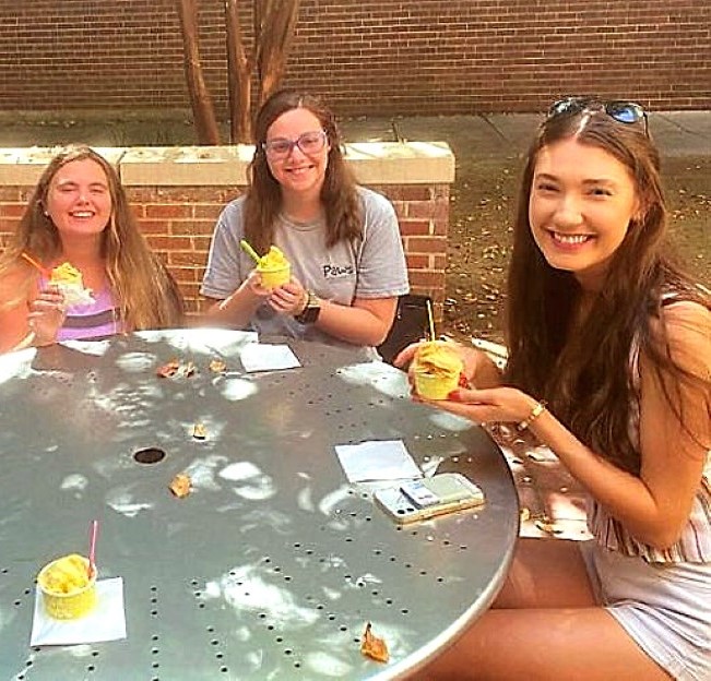 three students seated at a table eating Italian ice cream