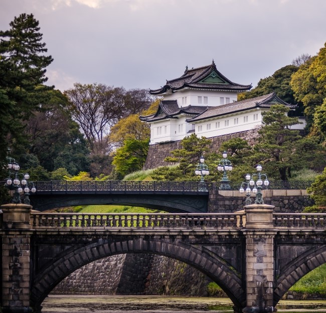 image of the Imperial Palace in the heart of Tokyo. It is a large, traditional Japanese structure set in a park with a lake and bridge