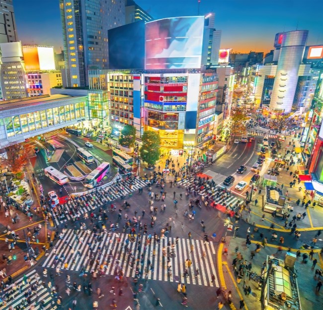 Top view of Shibuya Crossing at twilight in Tokyo, Japan. It shows a very busy urban street intersection with many cars and people