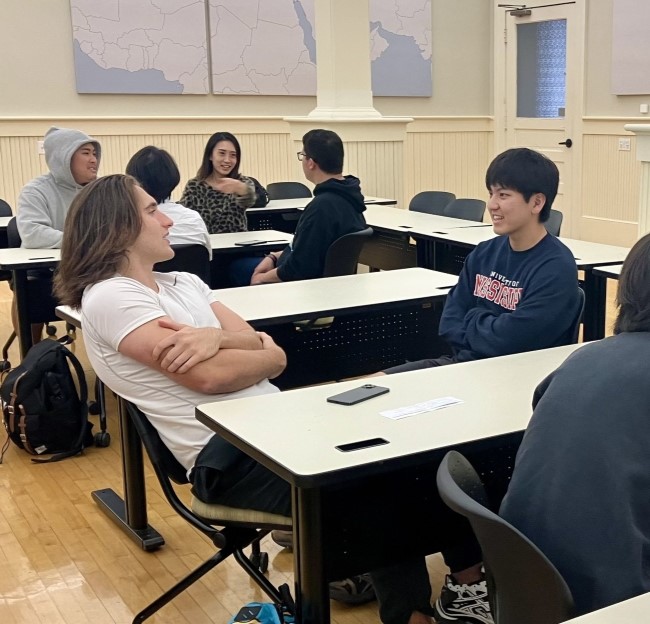 small groups of students seated together at tables while they practice speaking with Japanese students. 