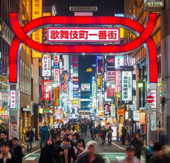 Neon lights and illuminated billboards of Shinjuku glittering at night above crowds of shoppers in the heart of Tokyo