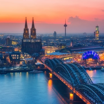 aerial view of Cologne, Germany at sunset with a river, bridge, and historic church