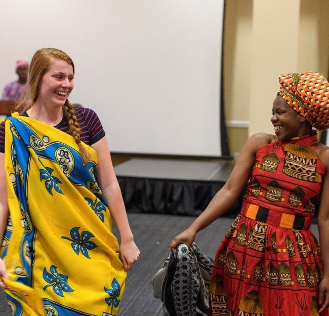 two students dressed in traditional African fabrics and walking in a fashion show