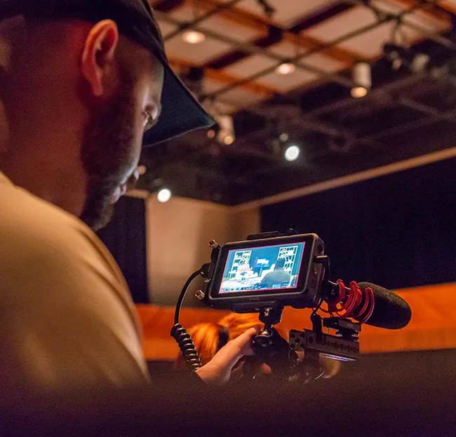 Man behind video camera looking into screen.