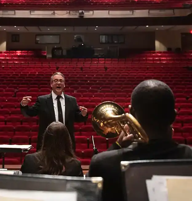 Jazz musicians on stage looking out to an animated conductor and an empty concert hall.