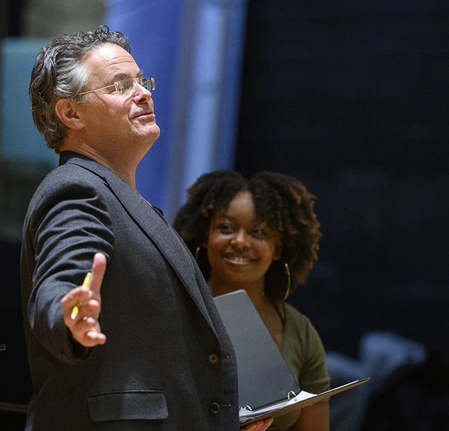 A professor poses and smiles dramatically on stage with a student