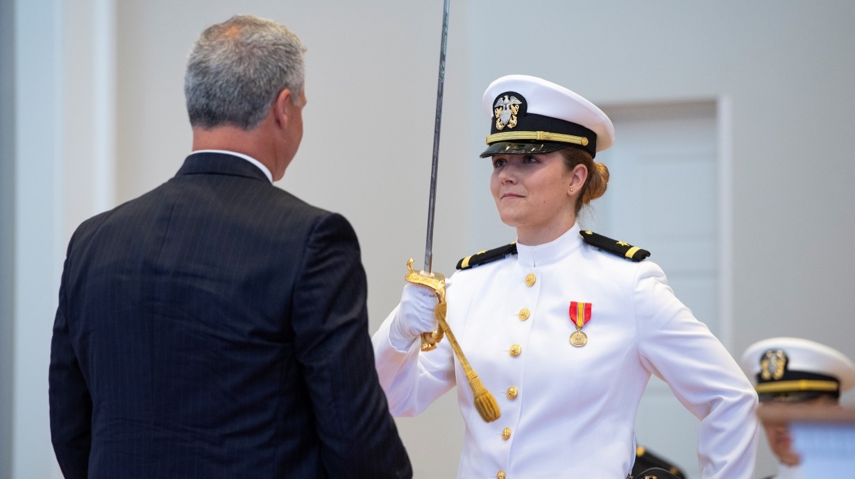 image of student at commissioning ceremony presenting sword in salute to family member