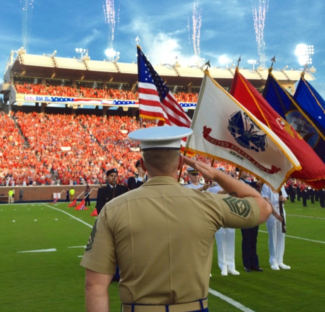 marine student in uniform giving a salute to a color guard on the football field