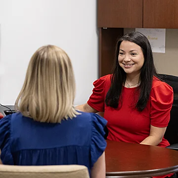 image of advisor seated at her desk and smiling at a student 