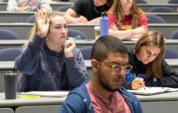 image of several students in a class, with one holding up her hand