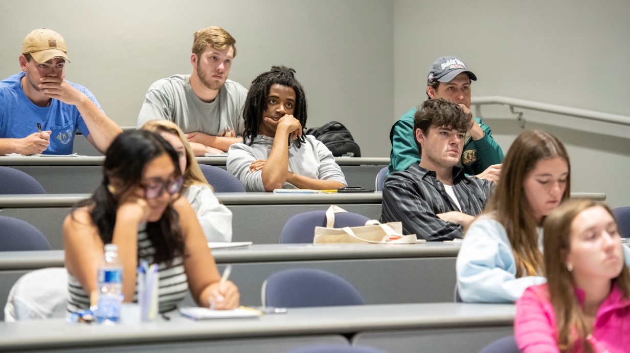 image of a small number of students seated in a classroom with serious faces as they listen to professor