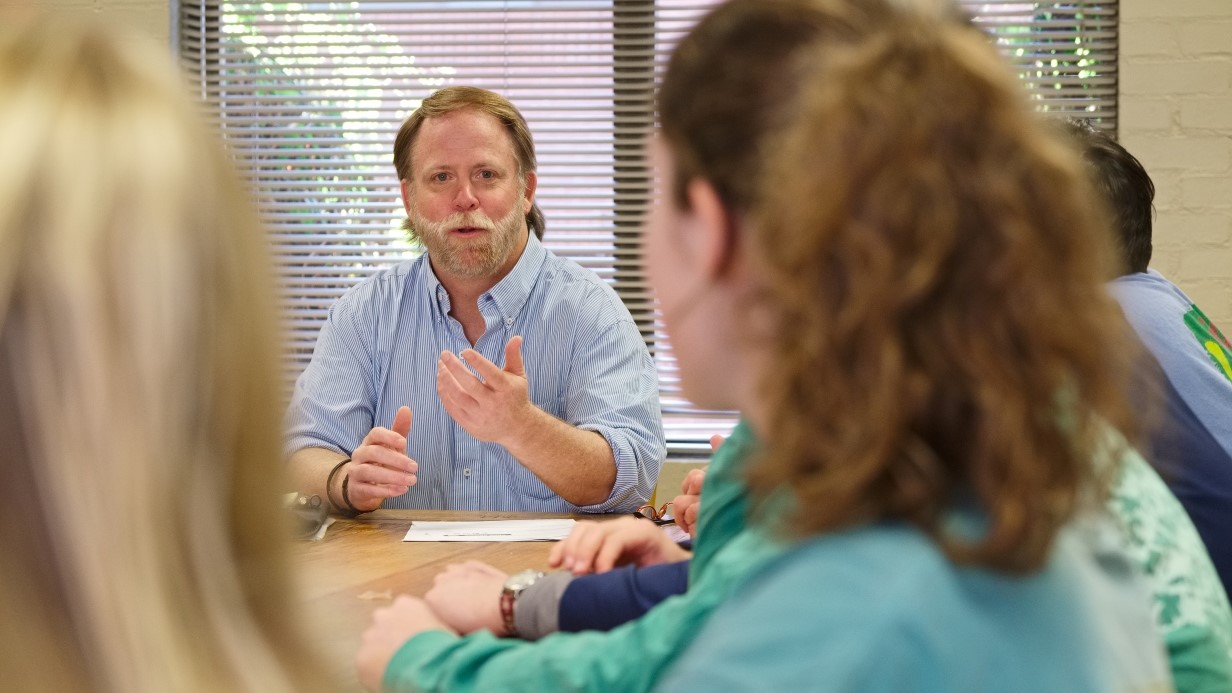 faculty member talking with students seated around a conference table