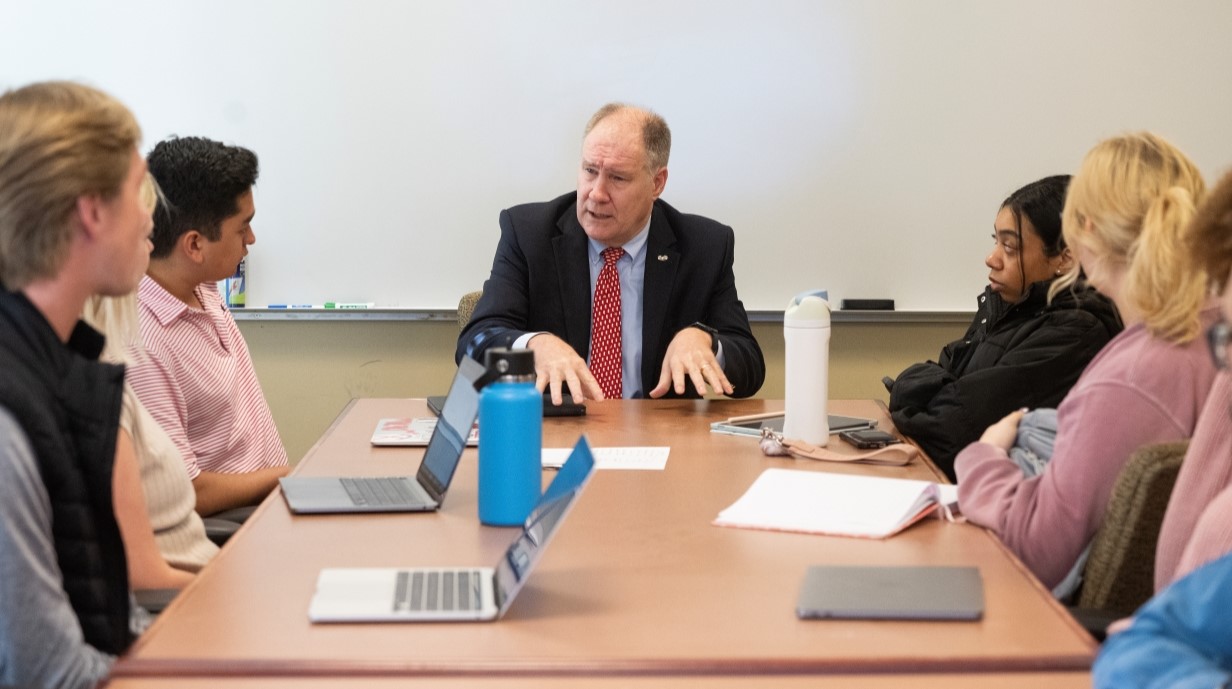 Congressman Trent Kelly seated at a table and talking with a class of students