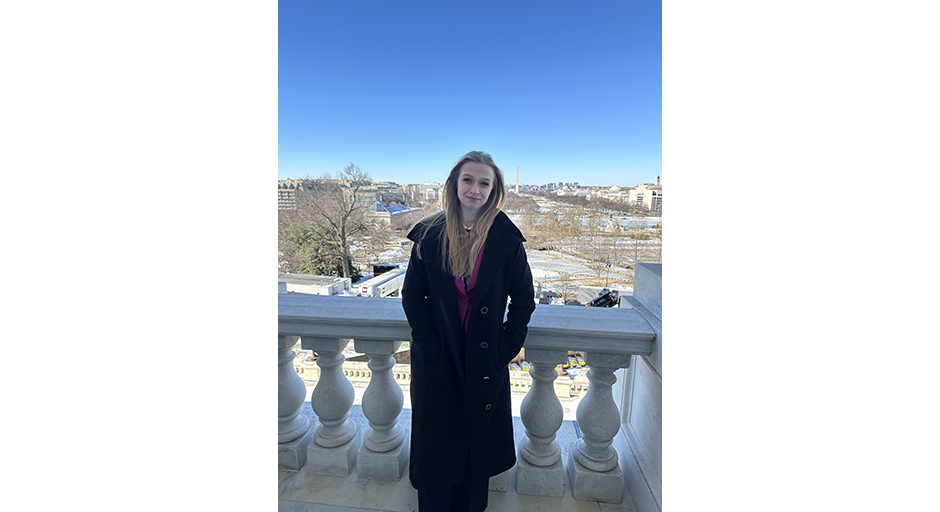 A young woman wearing an overcoat stands on a balcony overlooking a city skyline.