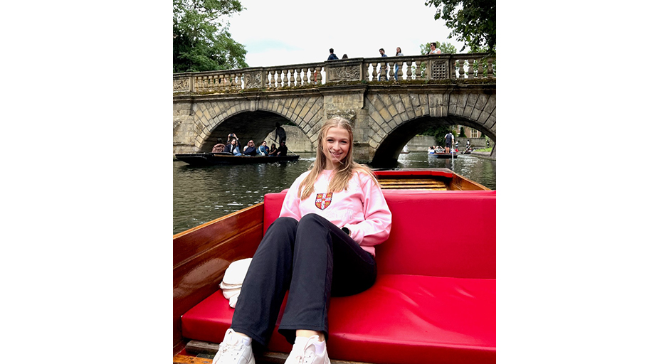 A young woman sits in a red paddleboat as it approaches a bridge.