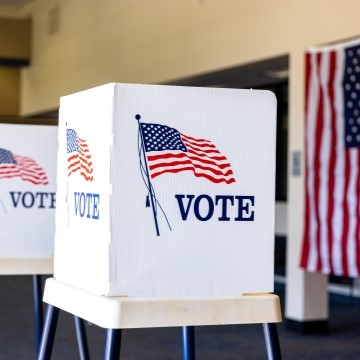 image of a voter booth with cardboard shields that have American flag and the word vote on the side