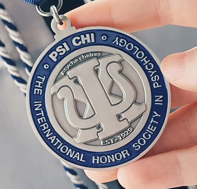 Up close shot of fingers holding a silver "Psi Chi" medallion