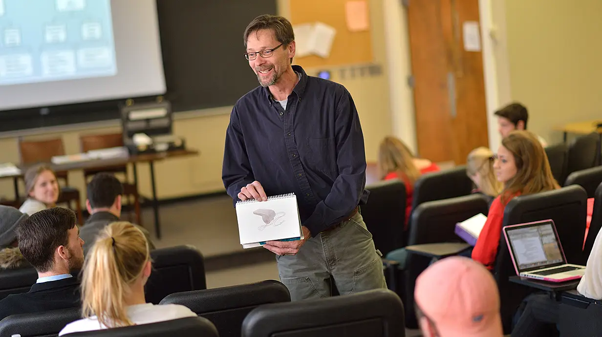 professor in the middle of a class holding up a drawing of a whistle for students to see.