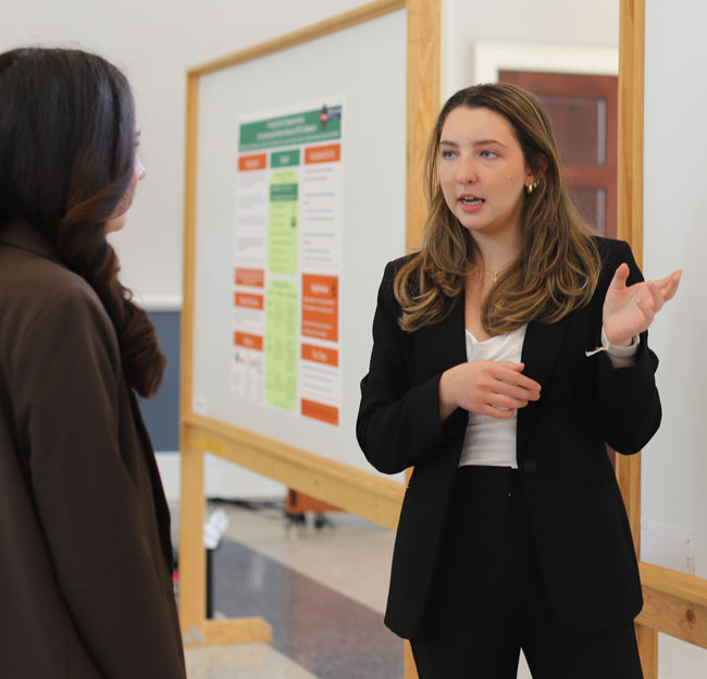 two students talking together with a research poster on a board nearby