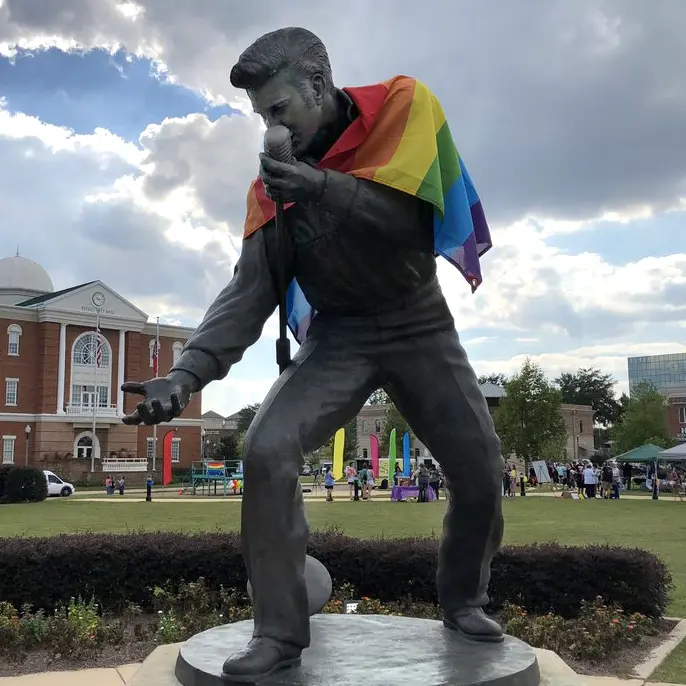 bronze statue of elvis with rainbow flag draped over shoulders
