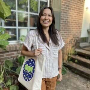 portrait of Alexandra Santiago standing outside of a storefront holding a canvas bag