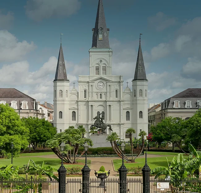 historic white building with black spires, a clock, and bronze sculpture of a man on a horse in front