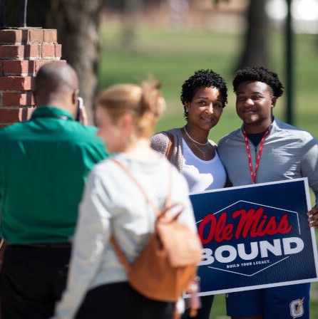 students holding ole miss bound sign under walk of champions arch