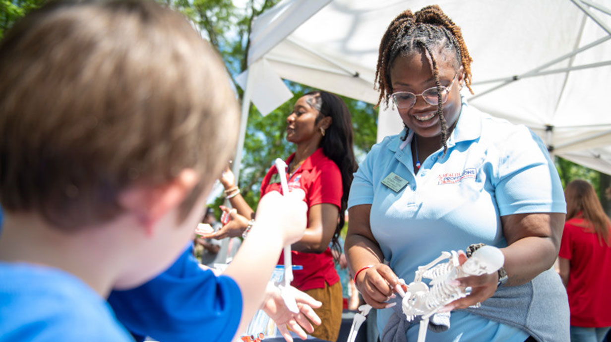 A University of Mississippi student outlines the highlights of a skeleton's anatomy to a young community member