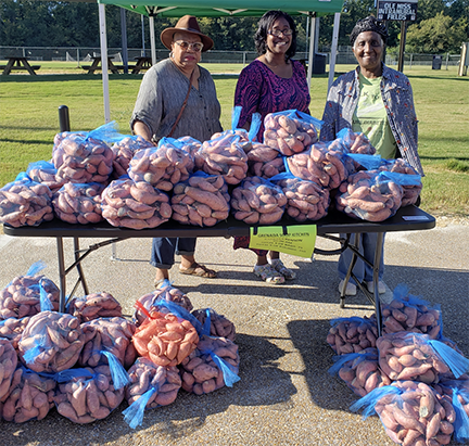 People next to bags of sweet potatoes.