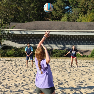 three students playing sand volleyball