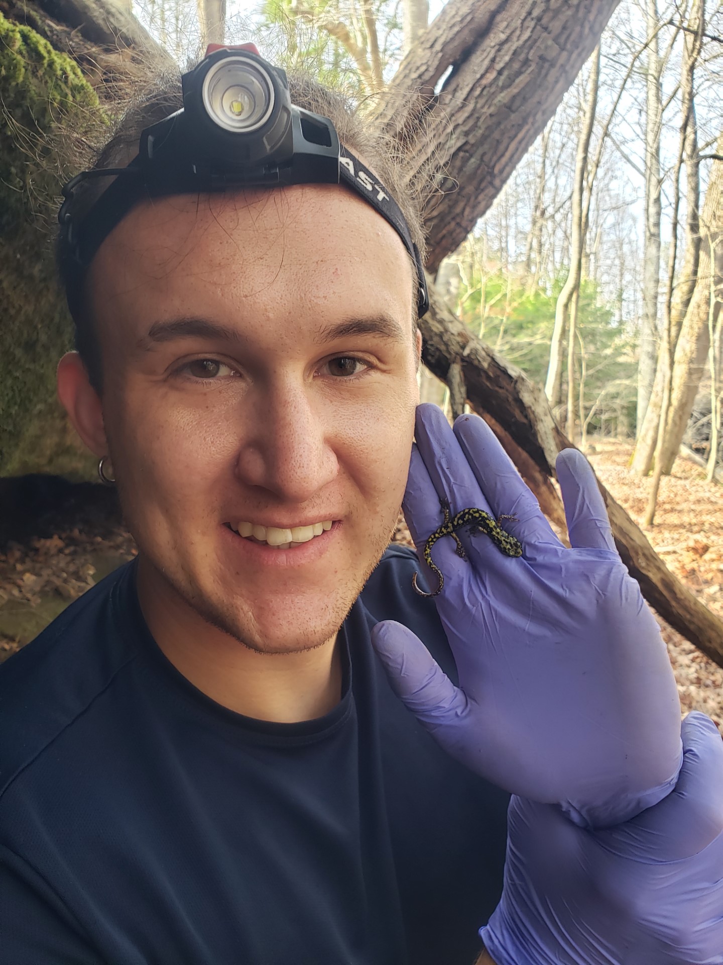 Headshot of Jakub Zegar wearing a headlamp and showing off a salamander on a gloved hand