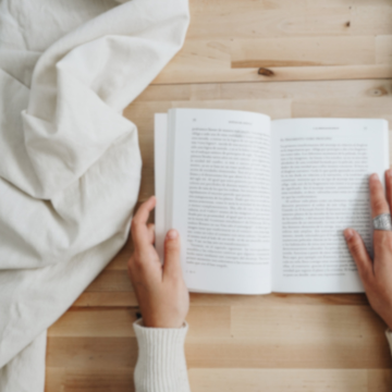 A person's hands hold open a book on a birch tabletop