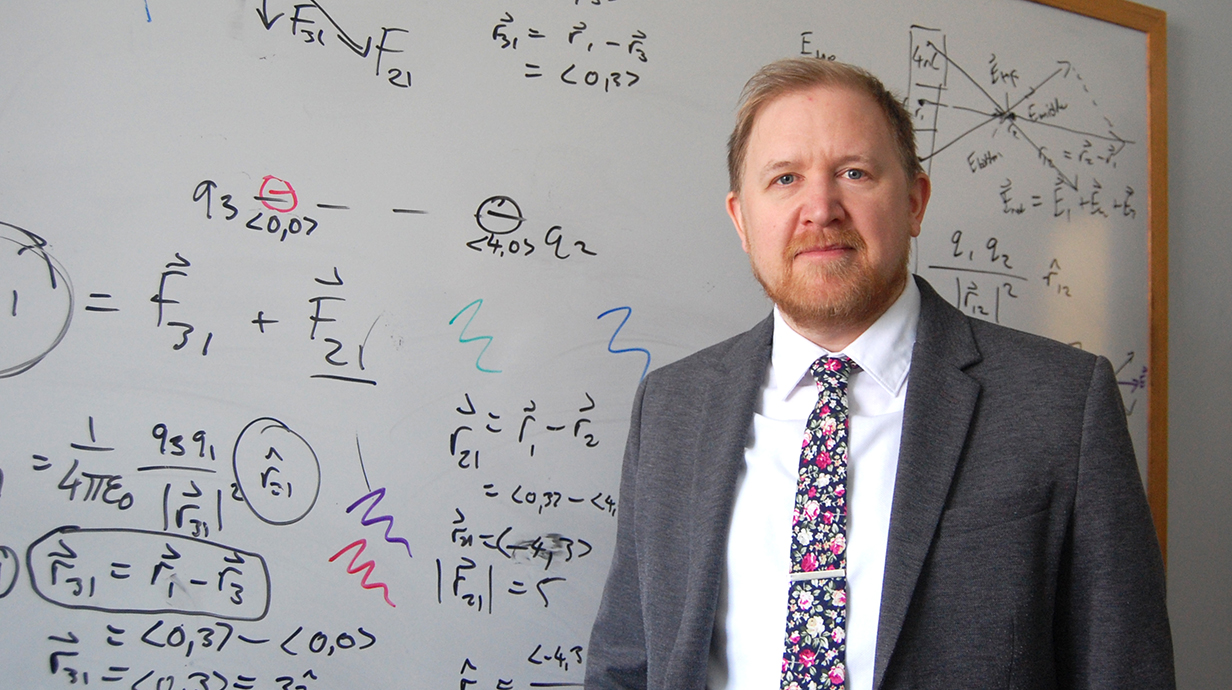 A man stands in ront of a white board full of complex equations.