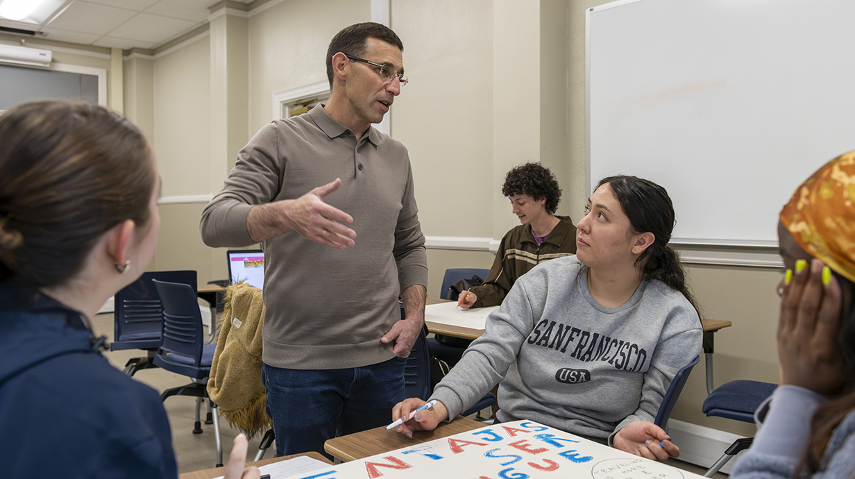 A teacher talks to a small group of students in a classroom.