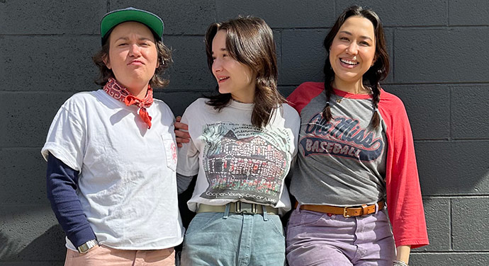 Three young women lean back against the outside of a building.