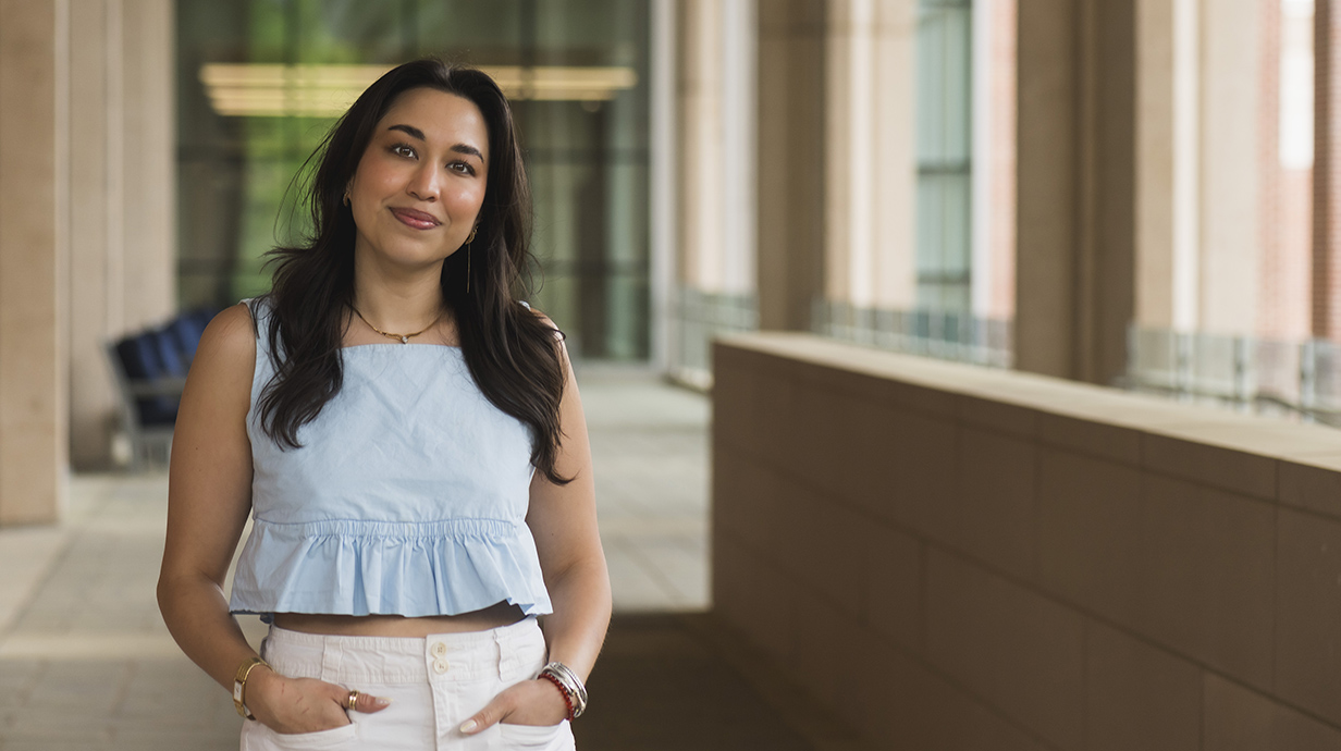 A woman stands with her hands in her pants pockets on a concrete plaza.