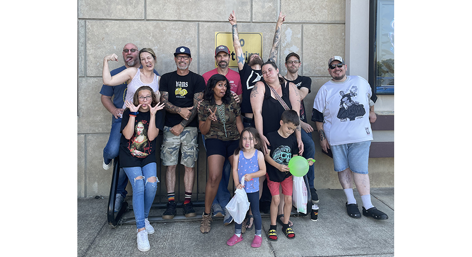 A large group of people stand against a concrete wall, all making funny faces.