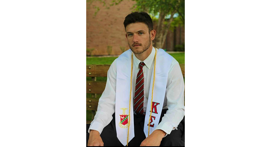 A man in a white shirt wears graduation regalia.