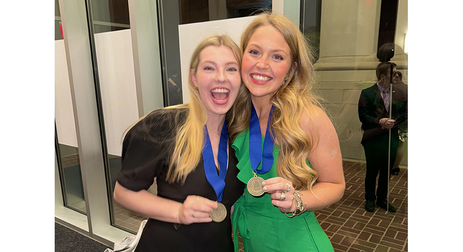 Two young women embrace and show off medals hanging from their necks.