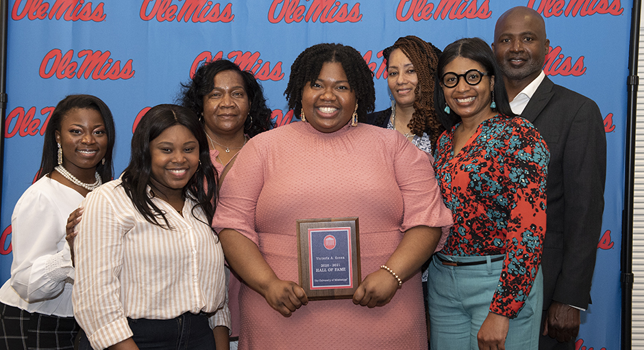 A group of people surround a young woman holding an award plaque.