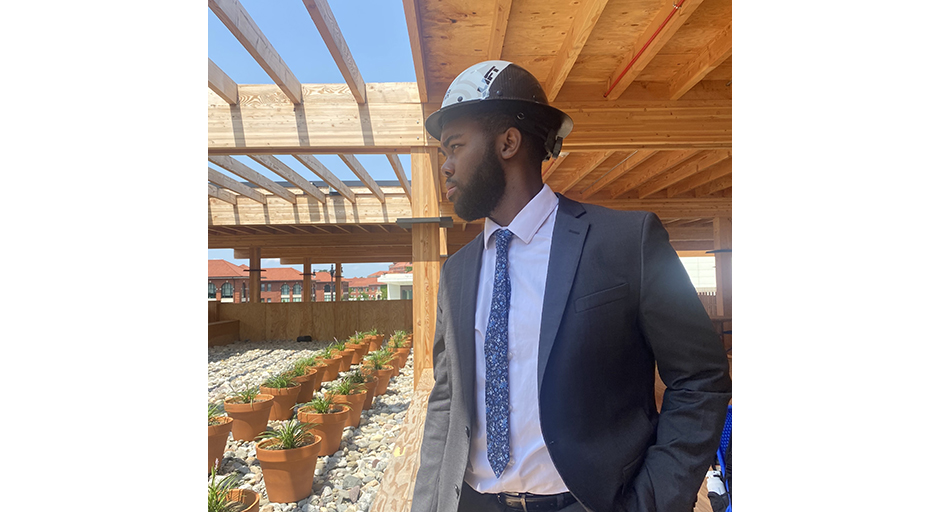 A young man wearing a suit and a hardhat looks over a construction site.