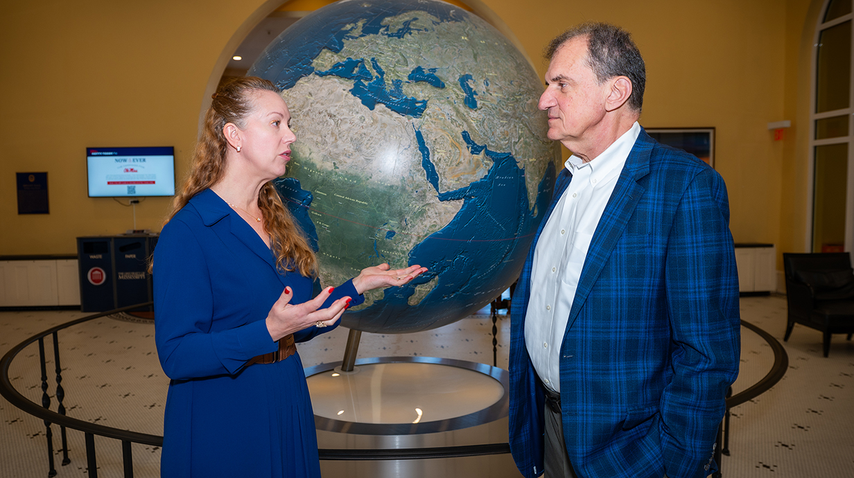 A woman and a man shake hands in front of a giant world globe.