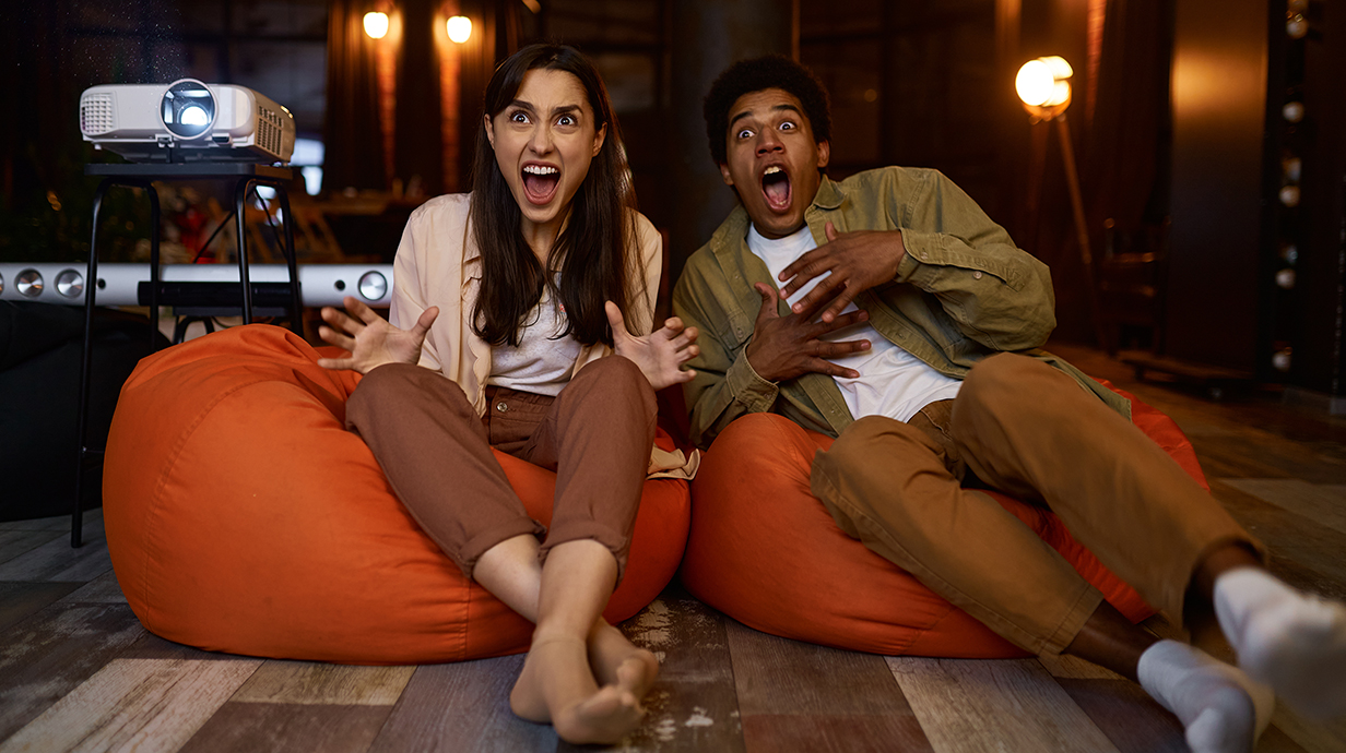 A young couple reacts with fright while watching a horror movie at home.