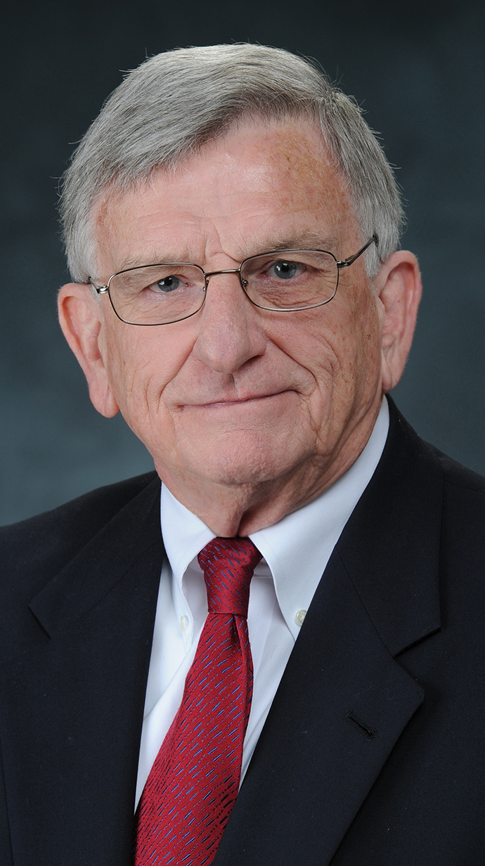 Headshot of a man wearing a dark suit and a red tie.