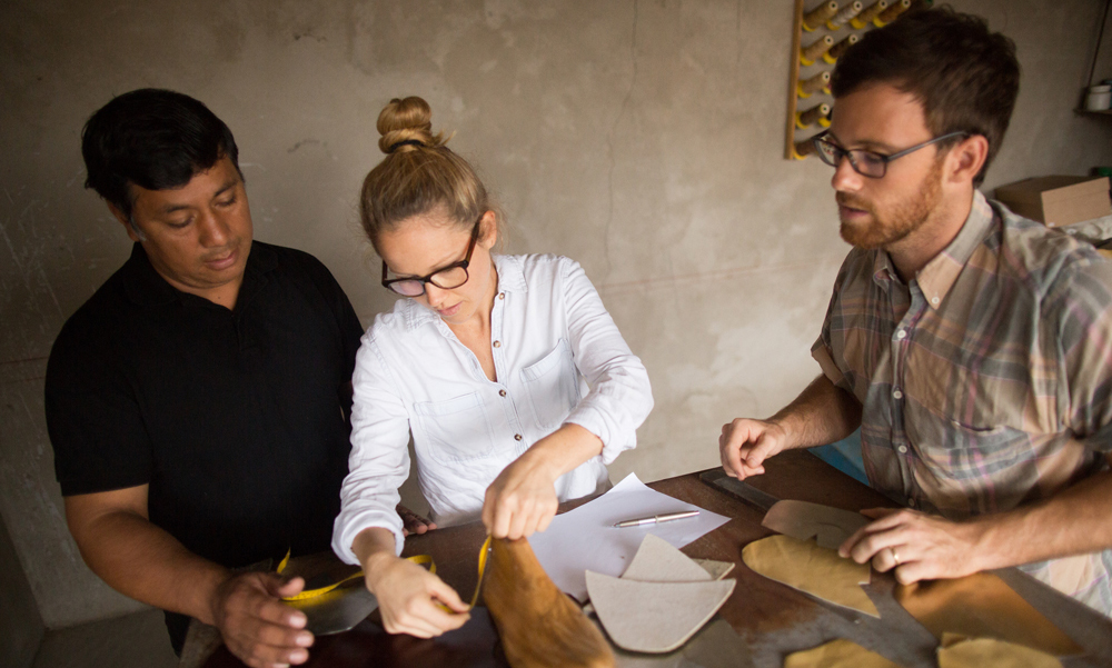 Two men watch as a woman measures a 3D model of a human foot.