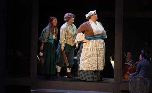 Three young women wearing costumes walk across a darkened stage.