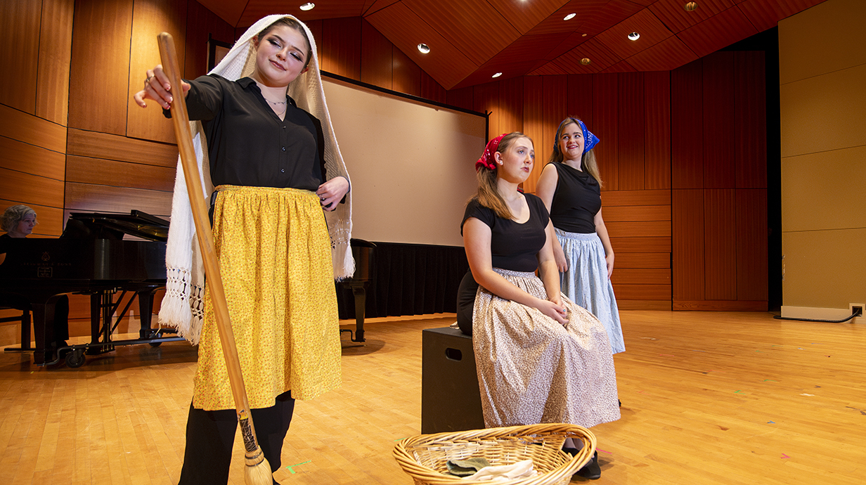 Three young women rehearse a scene on a stage.