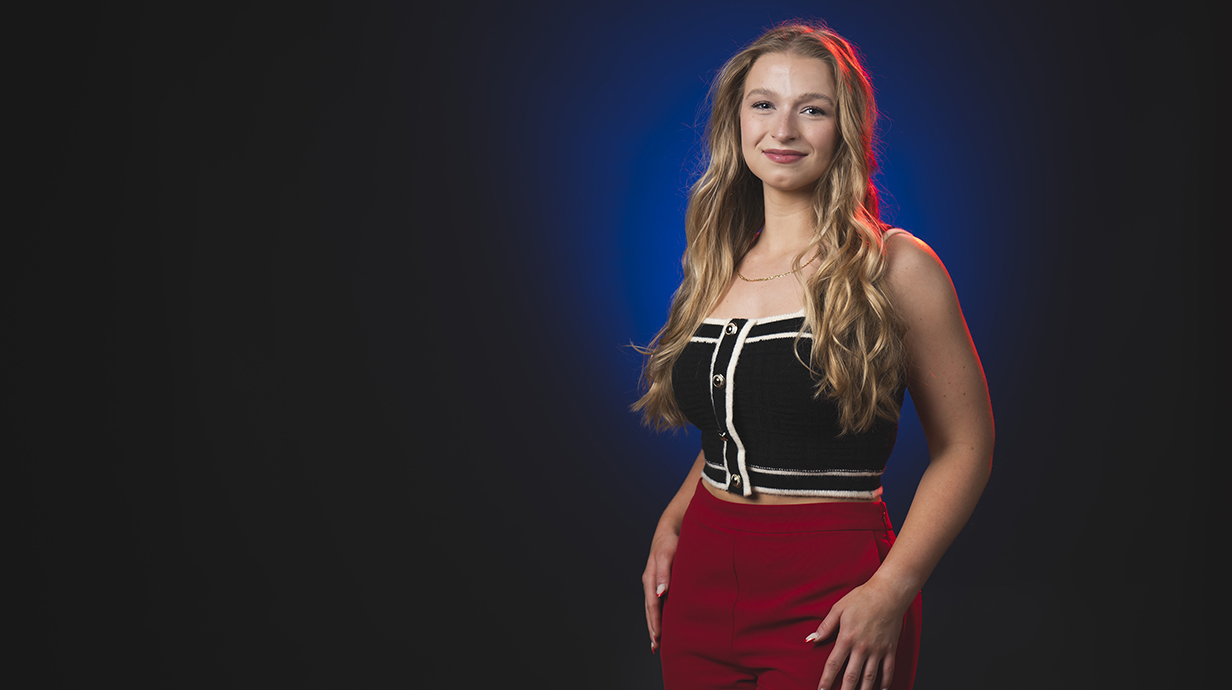 Portrait of a young woman standing against a dark blue background.