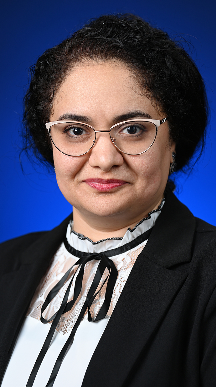 Headshot of a woman wearing a white blouse with a black string tie and black jacket.